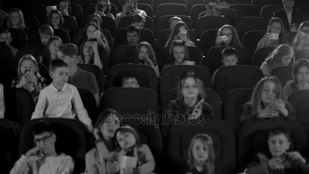 Niños felices en el cine mirando una caricatura y hacer flashes de teléfono. Tiro blanco y negro . — Vídeos de Stock