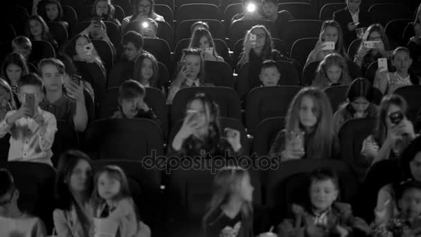 Niños felices en el cine mirando una caricatura y hacer flashes de teléfono. Tiro blanco y negro . — Vídeos de Stock