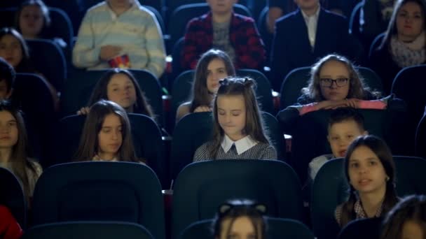 Όμορφο κοριτσάκι κοιτάζει τον εαυτό του σε αίθουσα κινηματογράφου. Πολλά παιδιά κάθονται. — Αρχείο Βίντεο