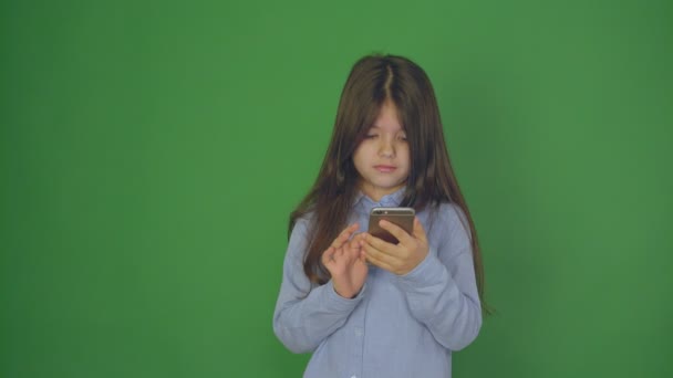 У маленькой девочки видеочат, видеозвонок на смартфон. Маленькая девочка машет и разговаривает с камерой телефона. Зеленый фон. close up — стоковое видео
