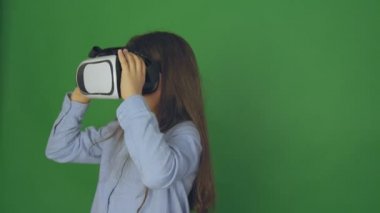 Yüksek kaliteli video sanal gerçeklik gözlüklü çocuk. Sanal gerçeklik bardaklarda mutlu kız loocing. Yeşil bir arka plan, kamera 4 k üzerinde küçük kız.