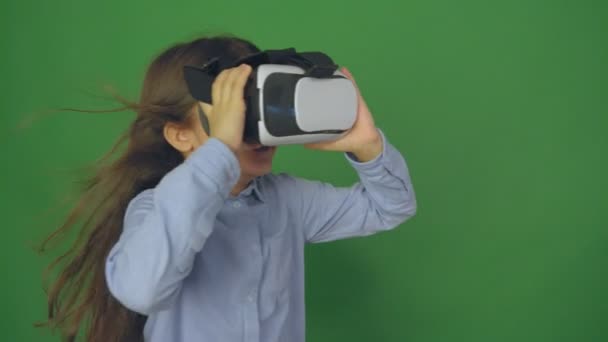 Cute little girl gesturing happily using VR virtual reality 360 degrees glasses. Girl on a green background. — Stock Video