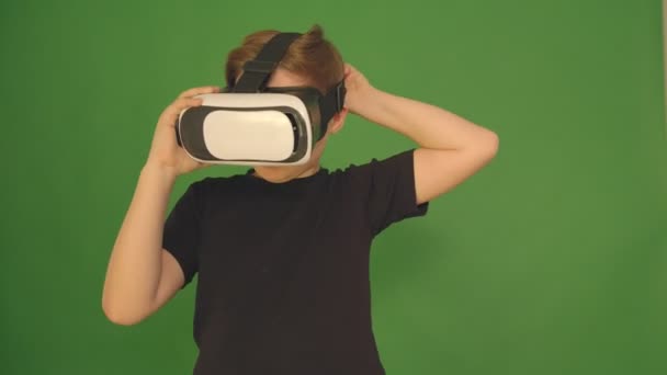 Junge in vr Brille. Nahaufnahme. Der Junge sieht emotional virtuell aus. Kind vor grünem Hintergrund. Kamera in 4k. — Stockvideo