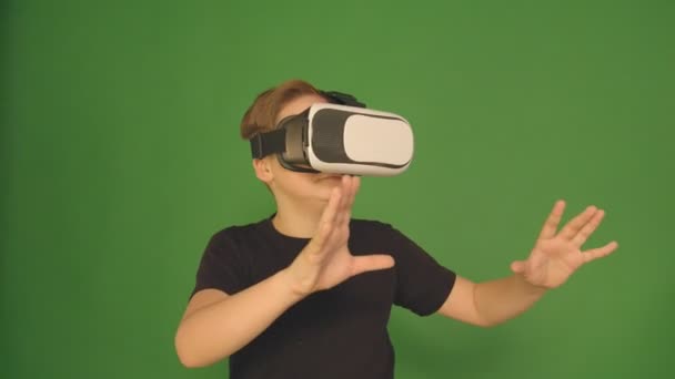 Cute Little Boy wskazując szczęśliwie za pomocą VR wirtualnej rzeczywistości 360 stopni okulary. Chłopiec w zielonym tle. — Wideo stockowe