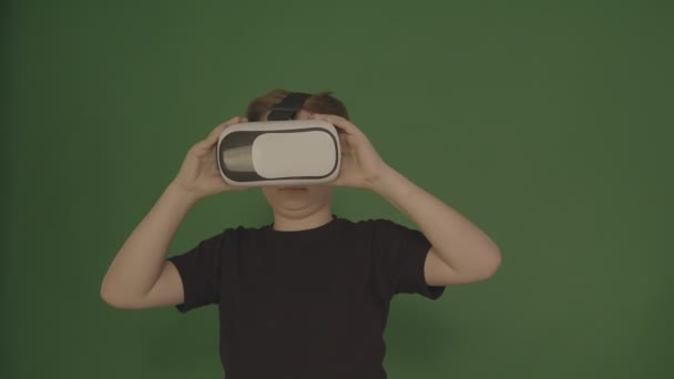 Lindo niño haciendo gestos felizmente usando gafas VR de realidad virtual de 360 grados. Niño en un fondo verde . — Vídeo de stock