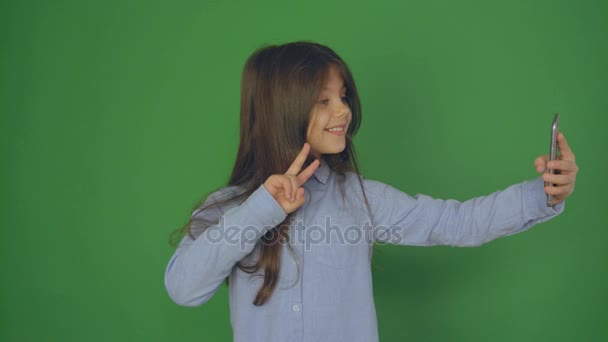 Niña usando el teléfono inteligente en una pantalla verde, hermosa niña haciendo selfie con el teléfono móvil en la mano, video cámara lenta . — Vídeos de Stock