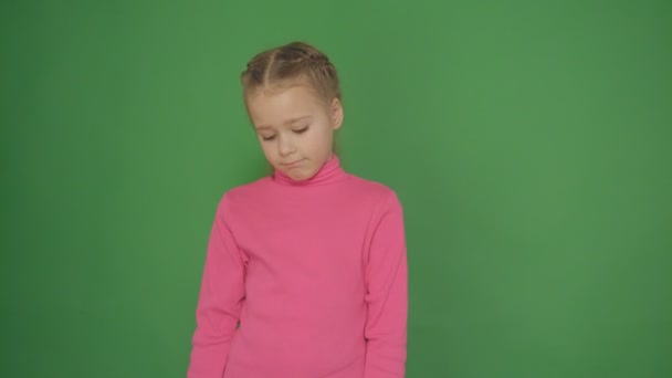 Närbild porträtt av en allvarlig liten flicka på en grön bakgrund. — Stockvideo