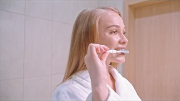Fiatal nő fogat mos a fürdőszobában, belenéz a tükörbe, élvezi a jó szájhigiéniát, felkészül a snowboardozásra — Stock videók