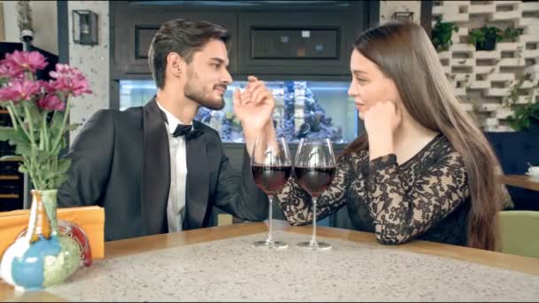 Молодий чоловік цілує руку красивої жінки, на столі два келихи вина. На підлозі є сноуборд . — стокове відео