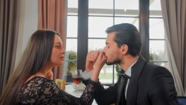 Casal jovem sentado a uma mesa em um café, o homem beija a mão de uma mulher bonita. Homem e mulher felizes olhando para o snowboard no chão — Vídeo de Stock