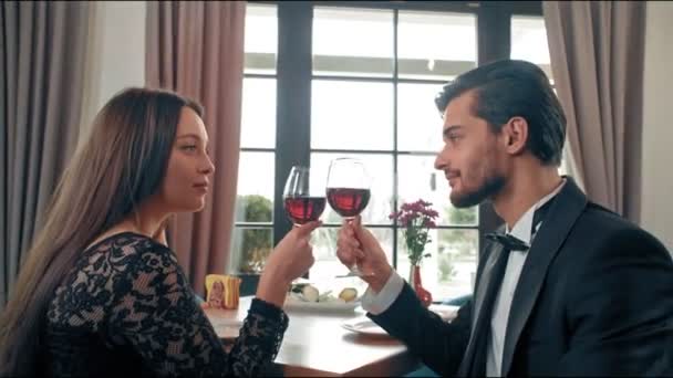 Casal jovem sentado a uma mesa em um café, em suas mãos copos com vinho tinto. Homem e mulher felizes olhando para o snowboard no chão — Vídeo de Stock