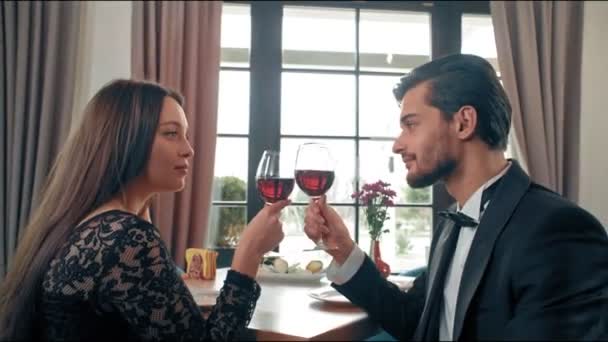 Young couple sitting at a table in a cafe, in their hands glasses with red wine. Happy man and woman looking at the snowboard on floor — Stock Video