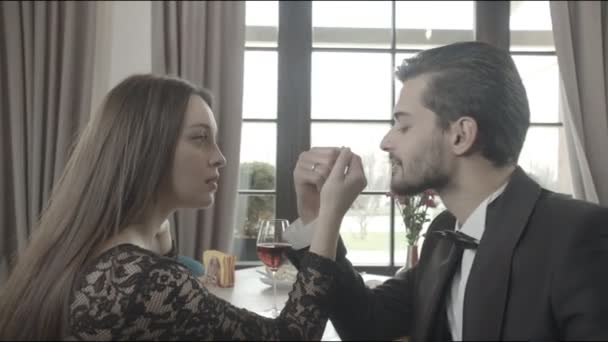 Unga par som sitter vid ett bord på ett kafé, mannen kysser en vacker kvinnas hand. Glad man och kvinna tittar på snowboarden på golvet — Stockvideo