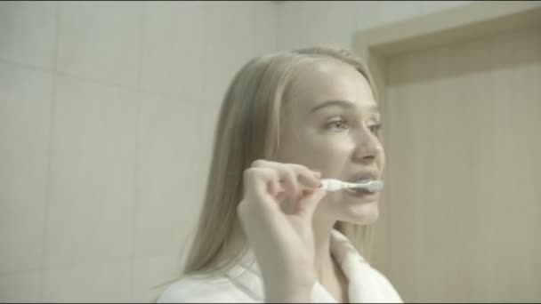 Mujer joven se cepilla los dientes en el baño, se mira en el espejo, disfruta de una buena higiene bucal, se prepara para el snowboard — Vídeo de stock
