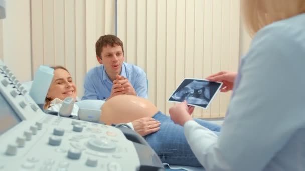Paar kijken naar echografie scan van baby in foto op de bank — Stockvideo