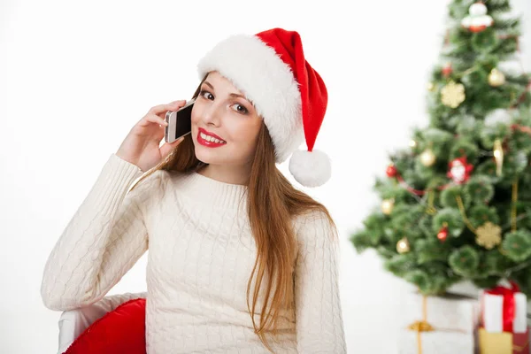 Girl in santa hat call phone by christmas tree — Stock Photo, Image
