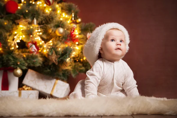 Happy baby wearing Santa hat over christmas tree — Stock Photo, Image