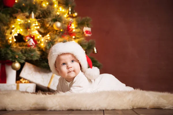 Happy baby wearing Santa hat over christmas tree — Stock Photo, Image