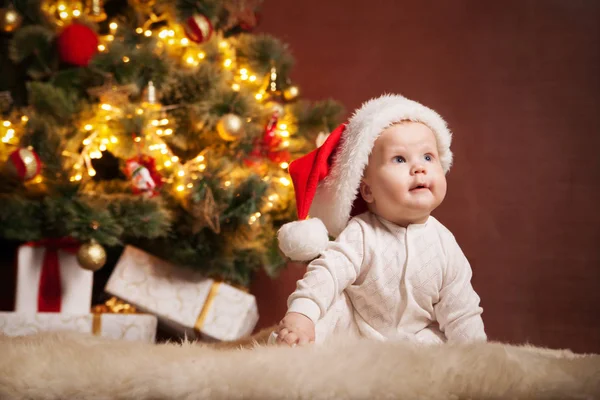 Happy baby wearing Santa hat over christmas tree Royalty Free Stock Photos