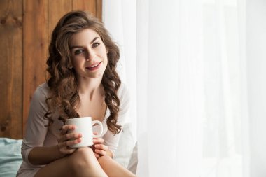 Pencereden Kupası ile gülümseyen kadın