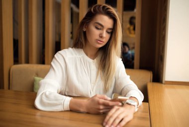 Bir kız bir kafede oturan ve telefonda yazarak bir smartphone kullanarak