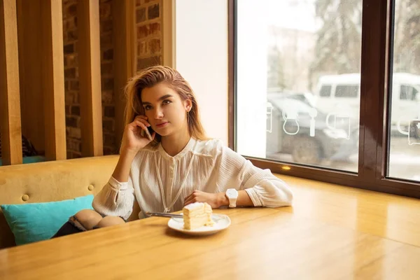 Una chica está sentada en un café y usando un teléfono inteligente, escribiendo en el teléfono — Foto de Stock