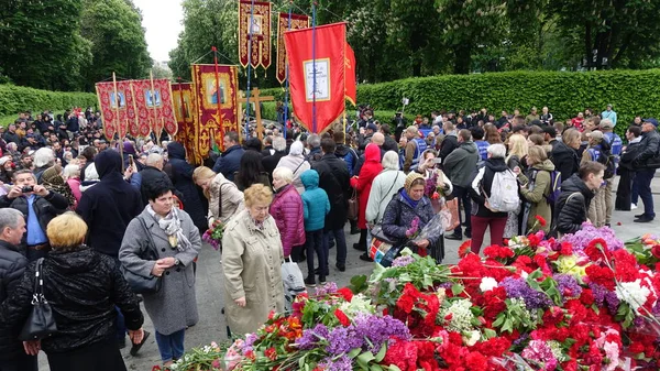 Im Kiewer Prachtpark bringen viele Menschen am Tag des Sieges Blumen zum Denkmal. Eine Prozession von Menschen mit orthodoxen Fahnen läuft zum Denkmal — Stockfoto