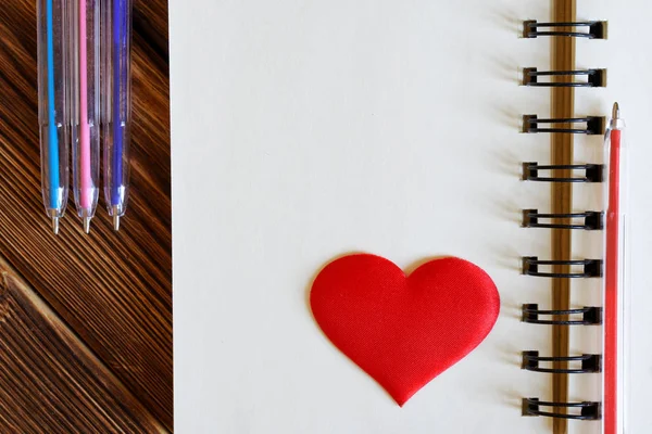 Red heart and multi-colored fountain pens next to a notebook. Bl — Stock Photo, Image