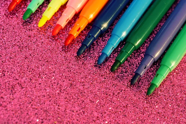 Lot of multi-colored markers on a bright sparkling lilac surface