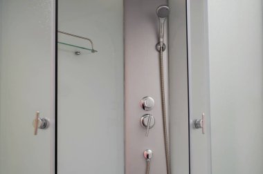 Krom musluğu olan duş kabini, şeffaf cam kapılar ve bir shel.