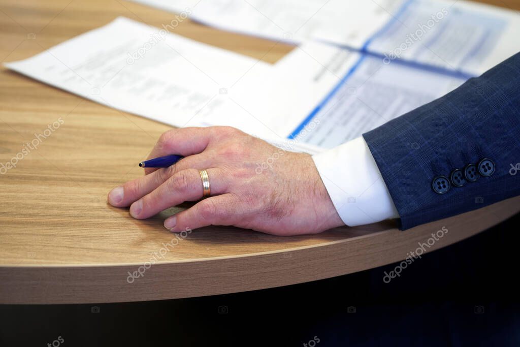 Hand of a male executive holding a fountain pen during a meeting or discussion. Decision making. Filling out documents, endorsement and signing. Close-up