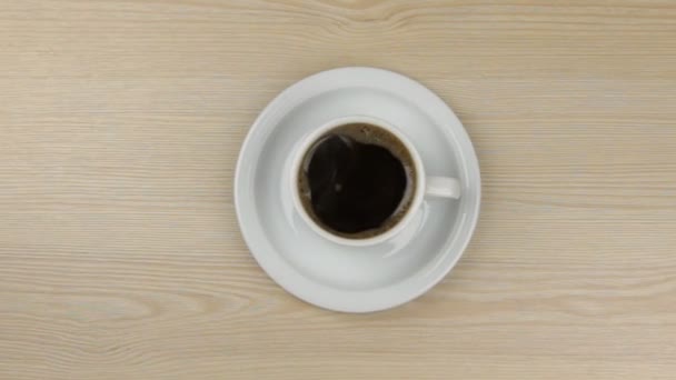 Onderlinge aanpassing van hete dampende kop koffie staande op een houten tafel — Stockvideo