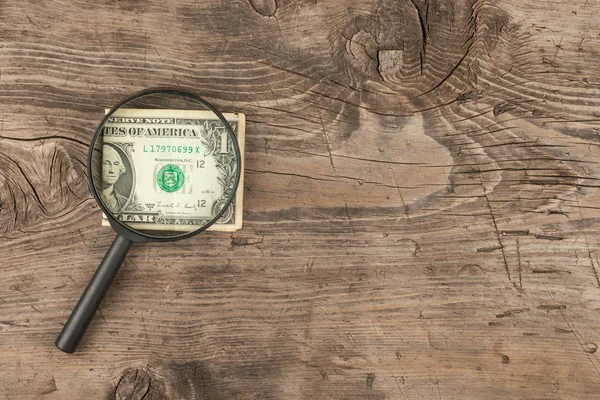 Magnifying glass is on the dollar bill  a wooden table. — Stock Photo, Image