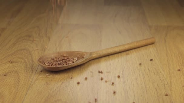 Grano de trigo sarraceno que cae sobre la cuchara de madera acostada sobre una superficie de madera . — Vídeo de stock