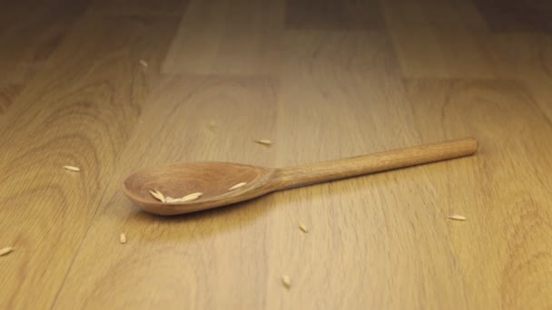 Grano de avena que cae sobre la cuchara de madera que yace sobre una superficie de madera . — Vídeo de stock