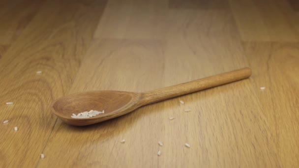 Grano de arroz que cae sobre la cuchara de madera que yace sobre una superficie de madera . — Vídeo de stock