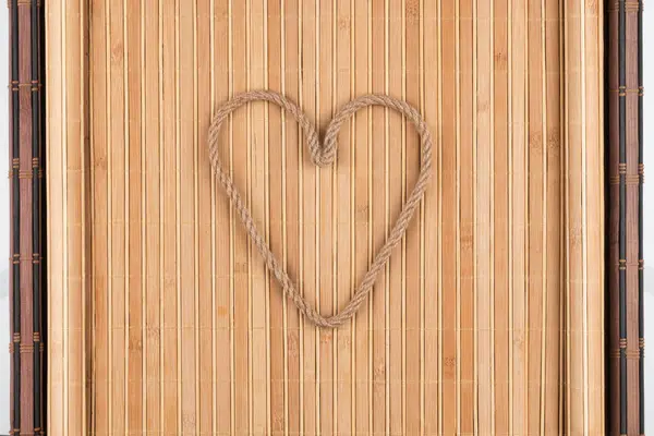 Coração simbólico feito de corda deitada em um tapete de bambu enrugado — Fotografia de Stock