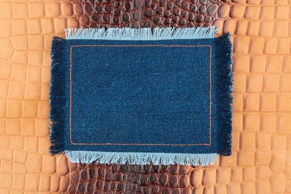 Frame made of denim with a fringe is on the brown crocodile skin — Stock Photo, Image