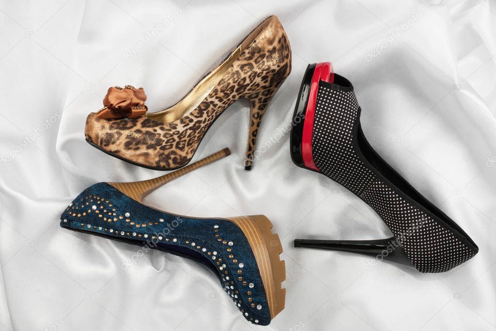 Three luxurious women's shoes with high heels lying on a white silk.