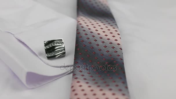 Primer plano de una corbata rosa y gemelos acostados sobre una camisa blanca . — Vídeos de Stock