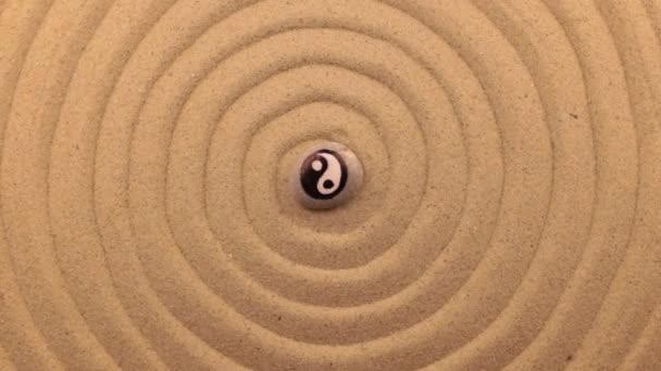 Rotação de uma pedra branca com um sinal yin-yang, deitado no centro de uma espiral feita de areia . — Vídeo de Stock