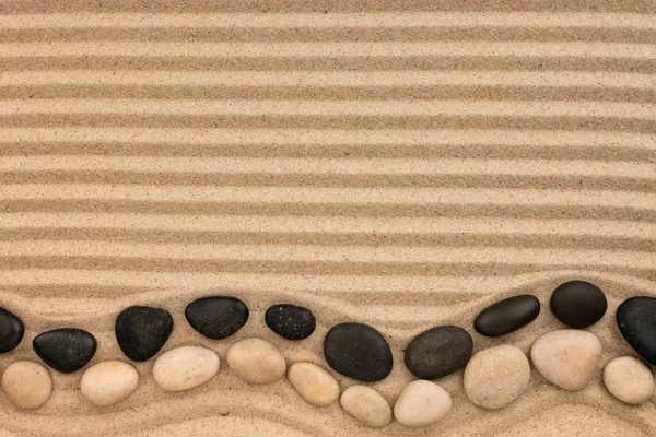 Two rows of stones, black and white lying on the striped sand, with space for text. — Stock Photo, Image