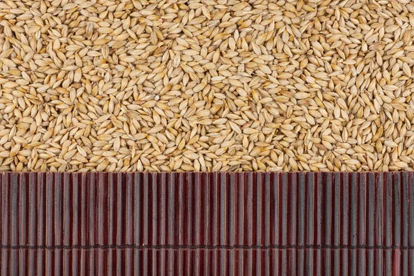 Beautiful bamboo mat on barley grains as agricultural background. — Stock Photo, Image