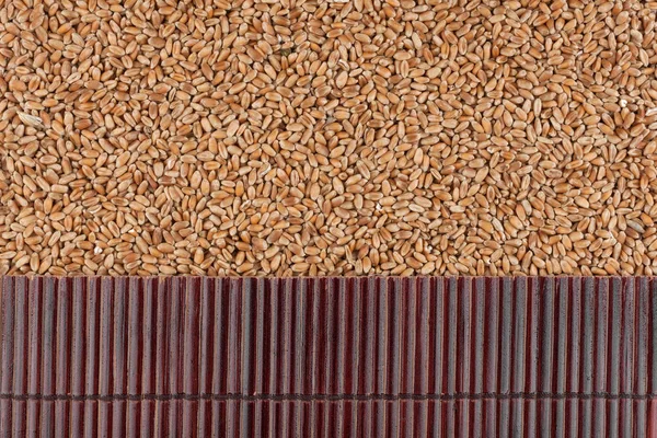 Beautiful bamboo mat on wheat grains as agricultural background. — Stock Photo, Image