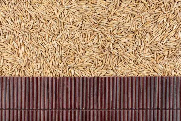Beautiful bamboo mat on oat grains as agricultural background. — Stock Photo, Image