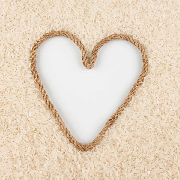 Rice grains and a rope in the shape of a heart with a place for designers. — Stock Photo, Image