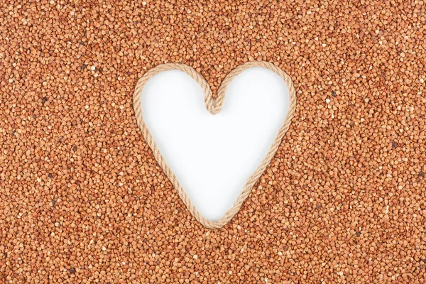 Buckwheat grains and a rope in the shape of a heart with a place for designers. — Stock Photo, Image