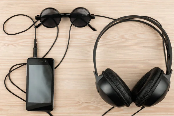 Sunglasses, phone and headphones lying on a wooden table, with space for your text. — Stock Photo, Image