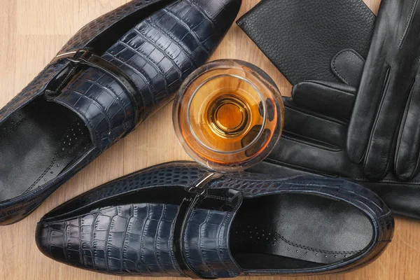 Classic men\'s shoes and glass of cognac, gloves and purse on wooden desk.