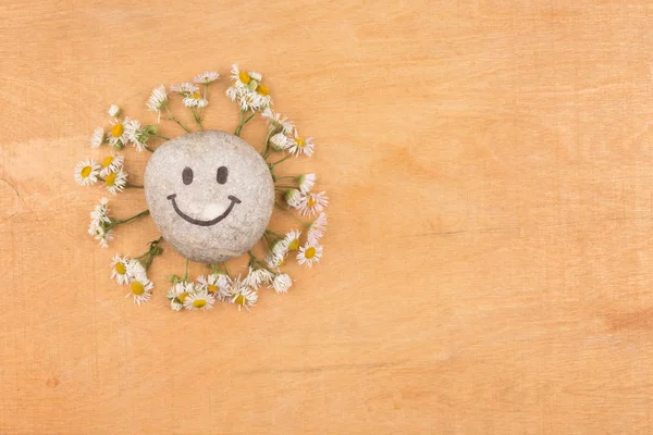 Smiley stone and daisies lying on a wooden surface. — Stock Photo, Image